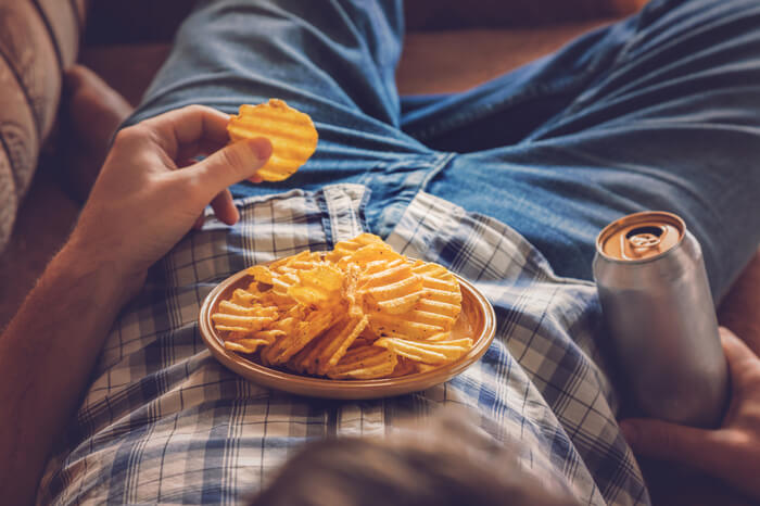 Binge Watching: Mann liegt in einem Sessel und isst Chips