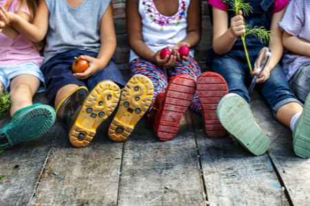 Vorschule für ärmere Kinder: Kids sitzen auf dem Boden und halten Gemüse in den Händen