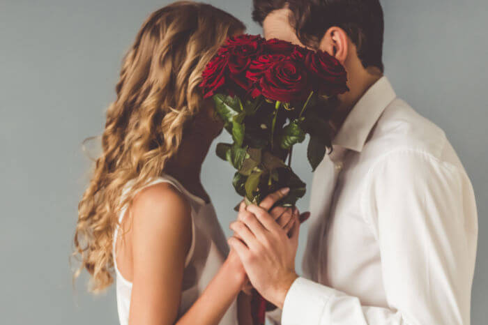 Valentinstag: Paar küsst sich hinter Rosen