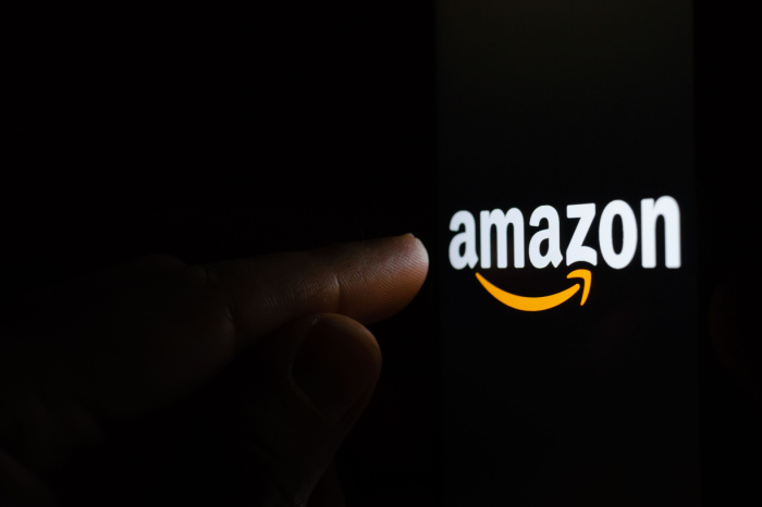 Finger zeigt auf Amazon-Logo auf schwarzem Hintergrund