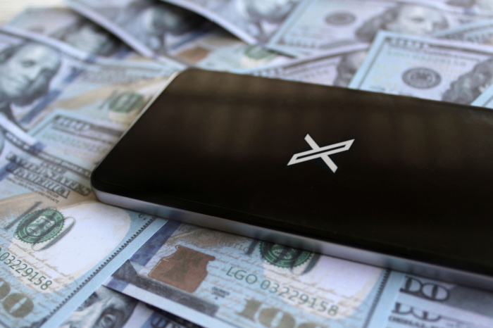 Smartphone zeigt X, liegt auf Dollar-Scheinen